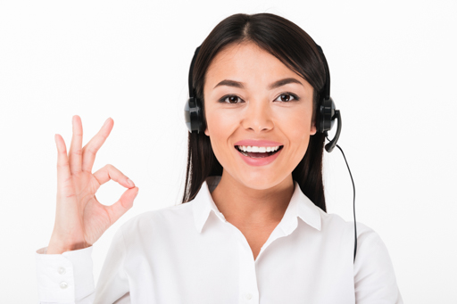 Close up of a cheerful asian woman in white shirt wearing headset with microphone showing ok gesture isolated over white background